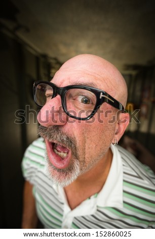 Wide angle color shot of a middle aged bald man with black glasses and a goatee looking with one eye into camera lens