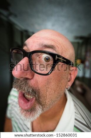 Wide angle color shot of a middle aged bald man with black glasses and a goatee looking with one eye into camera lens