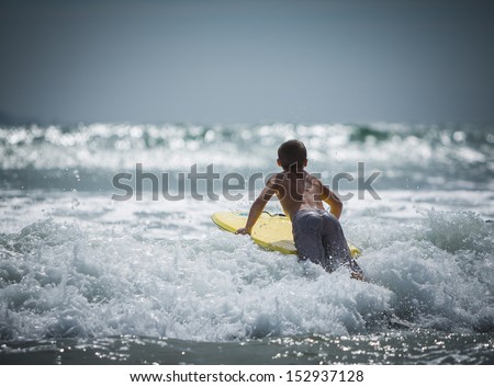 Young boy riding a yellow boogie board over a wave at Sunset Beach in Southern California