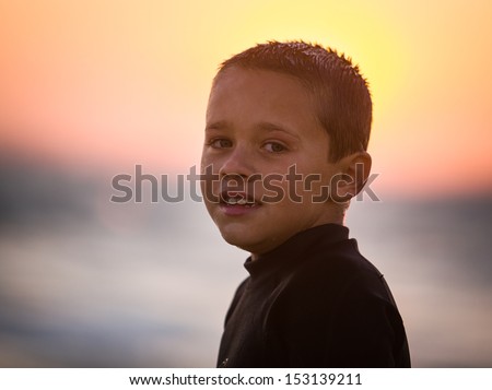Color head shot of young boy at the beach at sunset in a wet suit looking at camera
