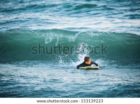 Young boy on a yellow boogie board looking back at a wave about to crash down at Sunset Beach in Southern California