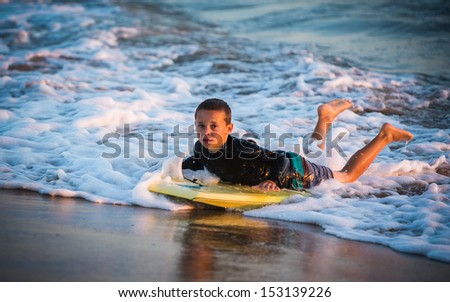 Young boy looking at camera riding a yellow boogie board to shore at Sunset Beach in Southern California