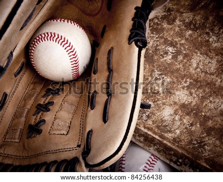 Close up of baseball glove with baseball in it laying on an aged home plate