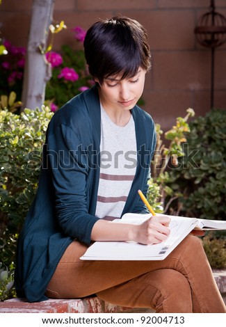 Young girl studying for test sitting on a wall with a textbook looking down at the pages