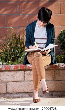 Young female student studying with highlighter in the back yard sitting on the wall
