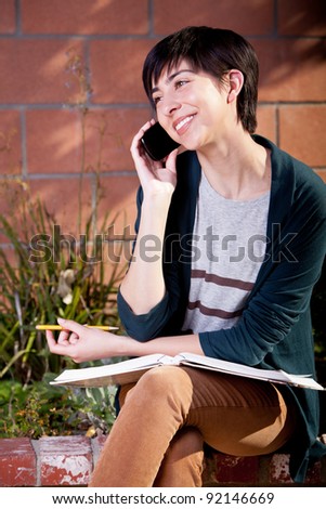 Young female student in the backyard studying on her cell phone