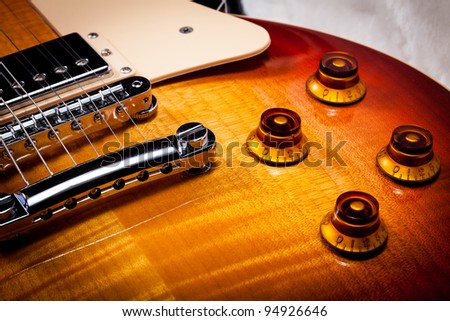 Close up of the Knobs the Pick Guard and Bridge of a Sunburst Electric Guitar