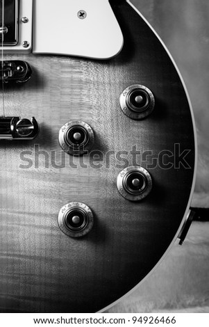 Black and White Close Up of the Corner of a Sunburst Electric Guitar with the Knobs, Pick Guard and PIckups