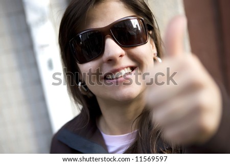 Portrait of beautiful casual woman with thumbs up - selective focus on the sunglasses