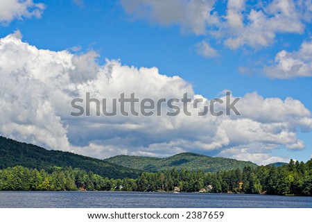 Mountains at the shoreline of a lake with large cumulus clouds in the sky above.
