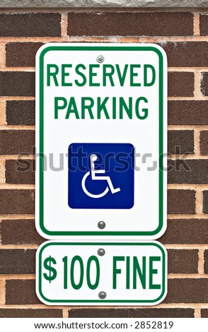 A reserved parking sign on a brick wall. There is a picture or symbol of a wheelchair on the sign along with a message for a one hundred dollar fine.