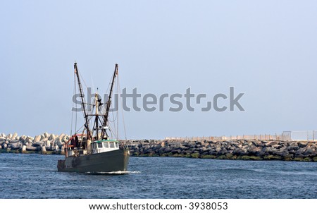 A boat in an inlet. There is a rock jetty behind the boat. Plenty of sky is showing which would make good copy space.