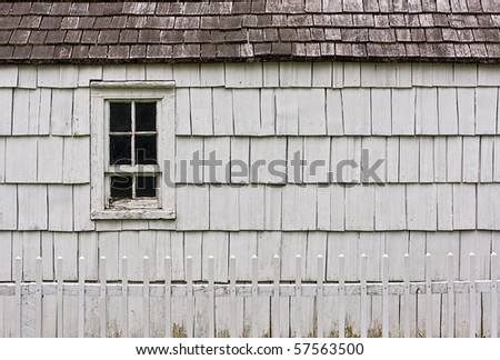 An old white building with a window as the focal point. There is a white picket fence in the foreground.