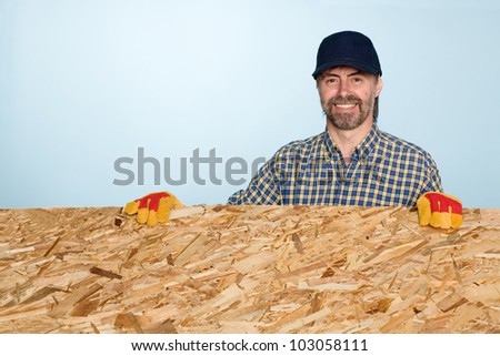 Smiling carpenter holds a sheet of plywood.