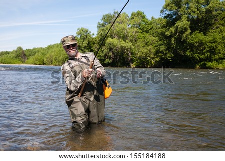 Joyful fisherman pulls caught salmon from the river.