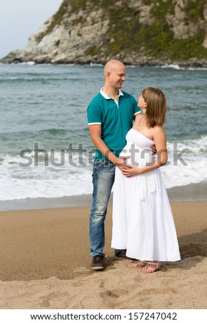 Happy pregnant woman and her husband strolling by the sea.