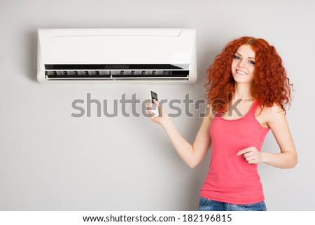Smiling red haired girl holding a remote control air conditioner.