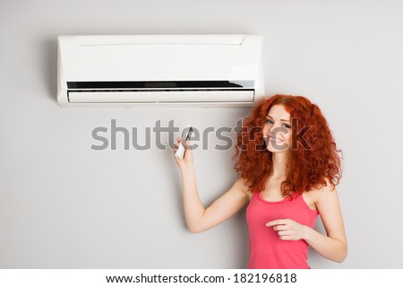 Beautiful red haired girl holding a remote control air conditioner.