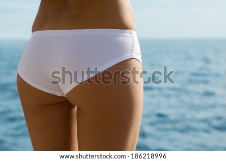 Girl with a slender figure in panties on a sea background.