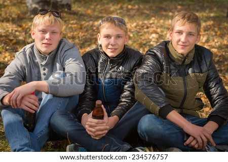 Group of guys with a bottle of drink in the autumn park, two of the boys twin brothers. Image with Instagram-like filter