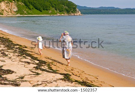 The grand daughter and the grandmother walk on a beach.