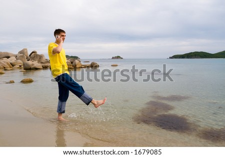 Coast.The young man talks on mobile and does(makes) splashes by a leg(foot).