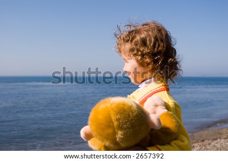 The little girl looks at the sea, in a hand the toy monkey.