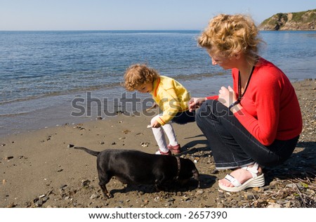 Mom and the daughter play with a dog(dachshund) at the sea.