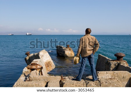 The young man stands on ruins of an old sea pier.