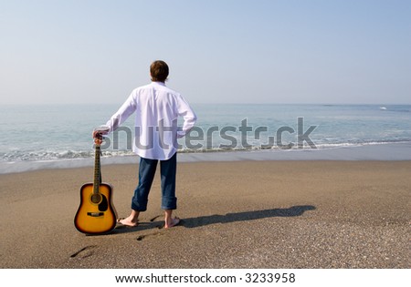 The young guy (musician) walks on a beach with a guitar.