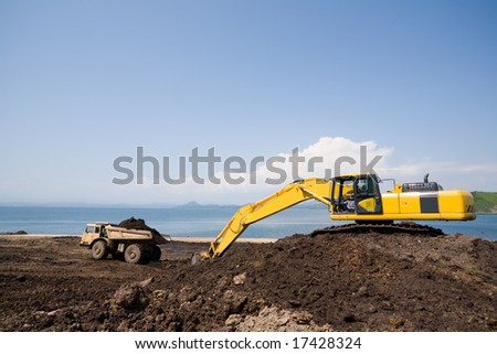 Construction of new seaport.Excavator loads a dump truck an earthen ground.