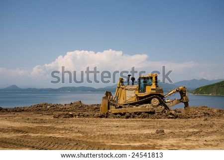 The bulldozer on a building site.On a background the sea.