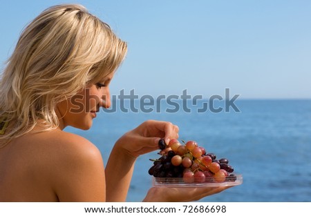 Attractive girl eating grapes at the beach by the sea.