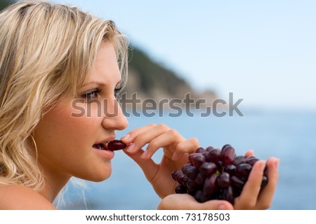 Young woman eating grapes at the beach by the sea.