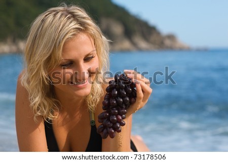 Beautiful girl with grapes on the beach by the sea
