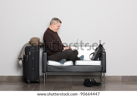 Elegant middle aged man uses a laptop. Waiting hall.