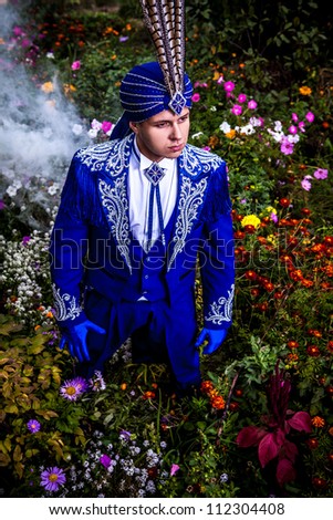 Man in expensive dark blue suit of illusionist pose on flower meadow.