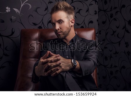 Handsome young man in dark suit relaxing on luxury sofa.