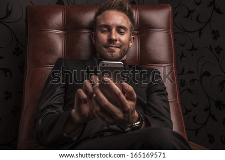 Handsome young business man in dark suit relaxing on luxury sofa.
