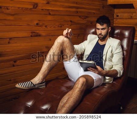 Handsome young man in white suit relaxing on luxury sofa with diary.