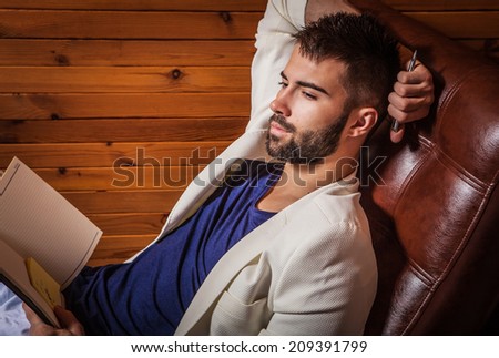 Handsome young man in white suit relaxing on luxury sofa with diary.