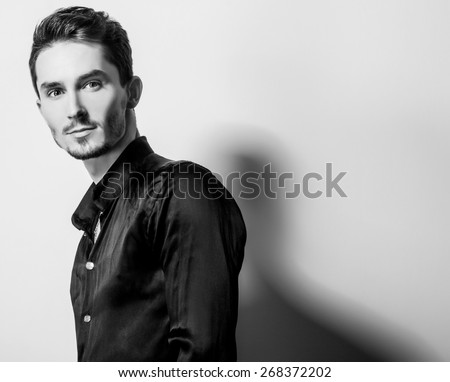 Elegant young handsome man in black silk shirt. Black-white studio fashion portrait.