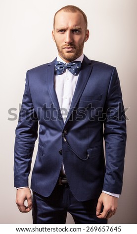 Elegant young handsome man in dark blue costume & bow tie. Studio fashion portrait.