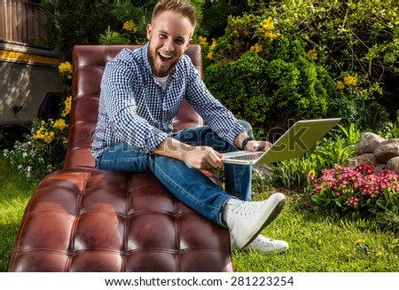 Young handsome man in casual clothes sit in luxury sofa with notebook in summer garden.