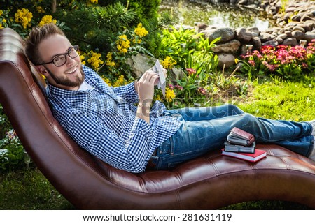 Young handsome man in casual clothes sit in luxury sofa with gift card in summer garden.