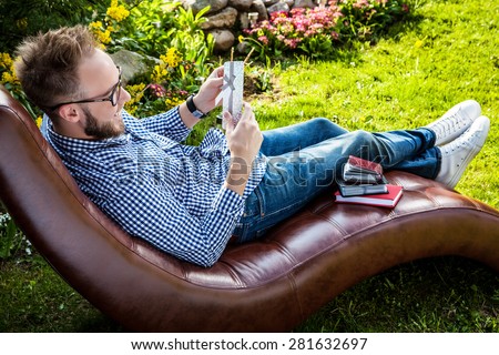 Young handsome smiling man in casual clothes & glasses with gift card relax in luxury sofa in summer garden.