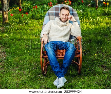 Handsome man relax in rocking-chair with plaid & phone in a summer garden.
