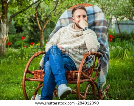 Handsome man relax in rocking-chair with cup of tea in summer garden.