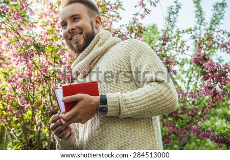 Young friendly man with red book in a summer garden at sunset.