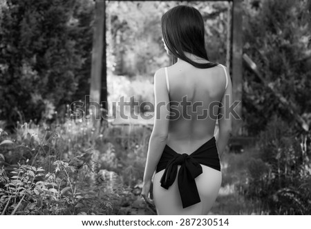 Beautiful young brunette girl in luxury dress posing from a back in summer garden.Black-white photo.